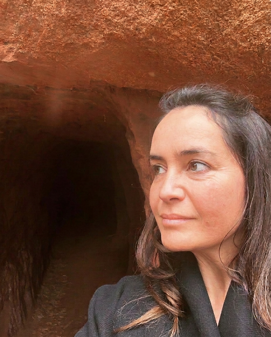 Retrato de Daniela Velho junto a uma gruta de terra ocre, com olhar sereno